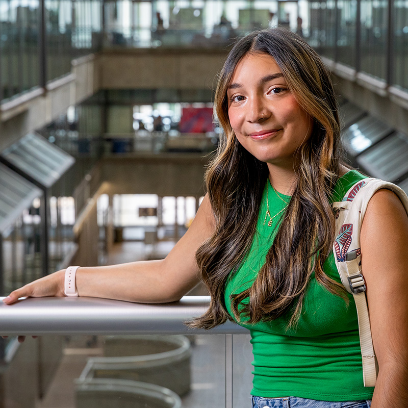 Martinez in a green shirt and backpack standing inside a modern building with glass railings.