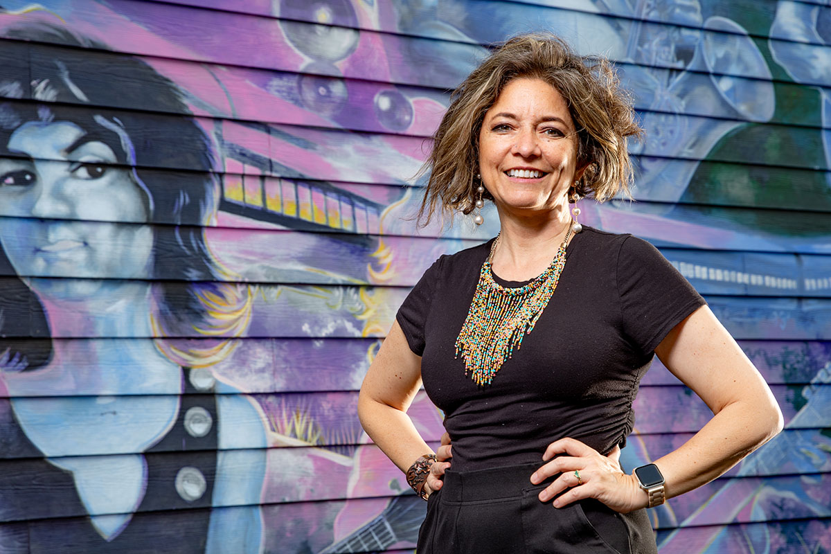 Dynamic street art of music icons and instruments frames a professor in colorful attire and ornate necklace.