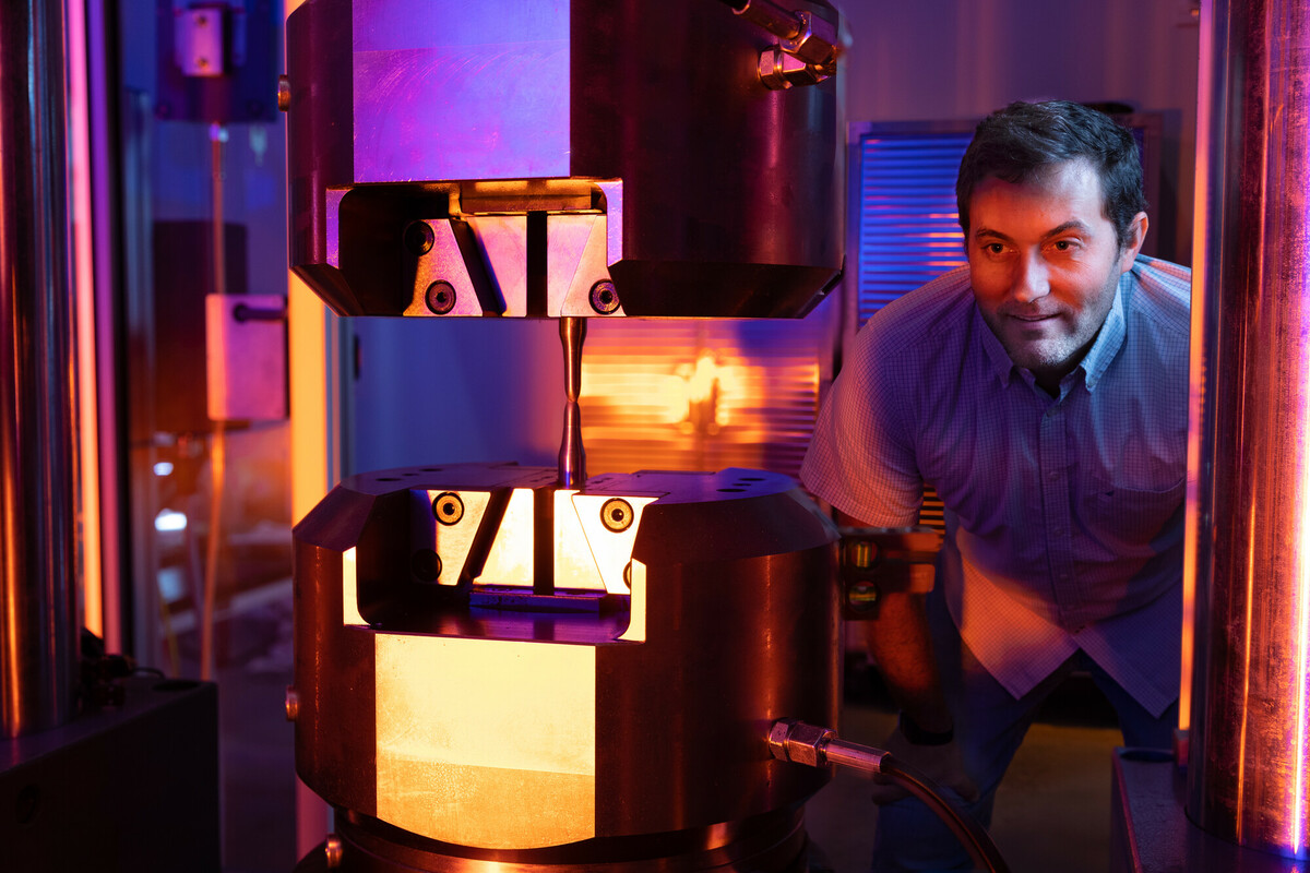 Engineer observing a tensile testing machine applying stress to a metal specimen in a lab.