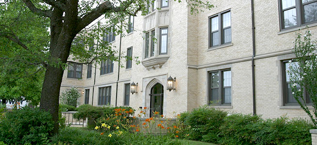 Student walks across campus at the start of fall. Leaves from the tree overhead are turning yellow and red.