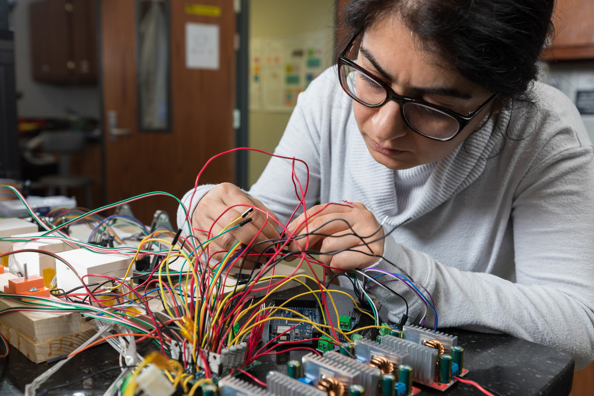 Researcher assembles a detailed electronic system with tangled wires and circuit boards on a lab workstation.