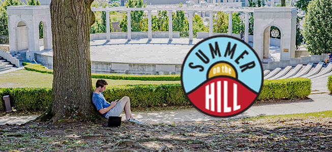 Student sits outside surrounded by trees on the University of Arkansas campus